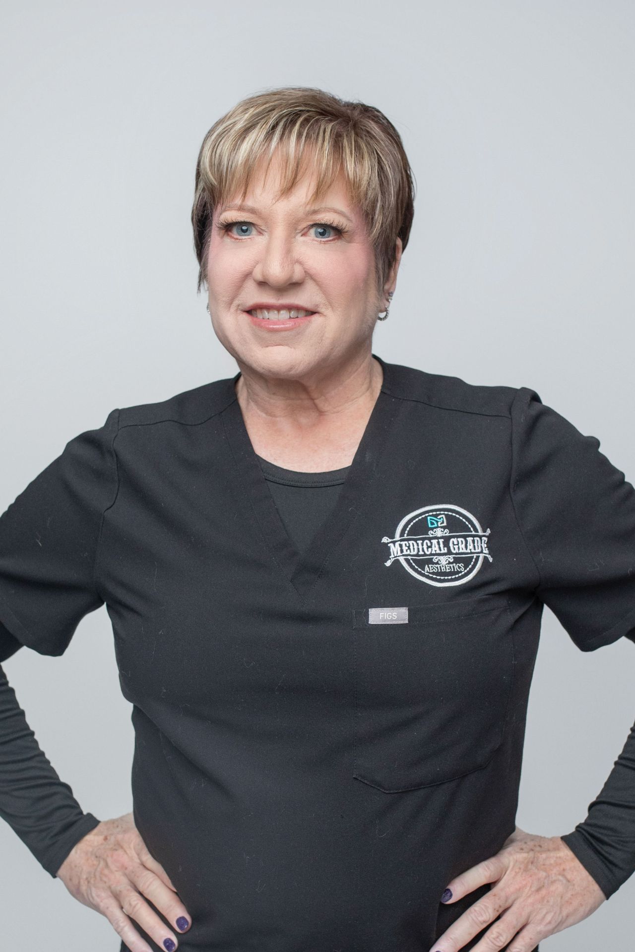 blonde woman with short hair smiling at camera with her hands on her hips