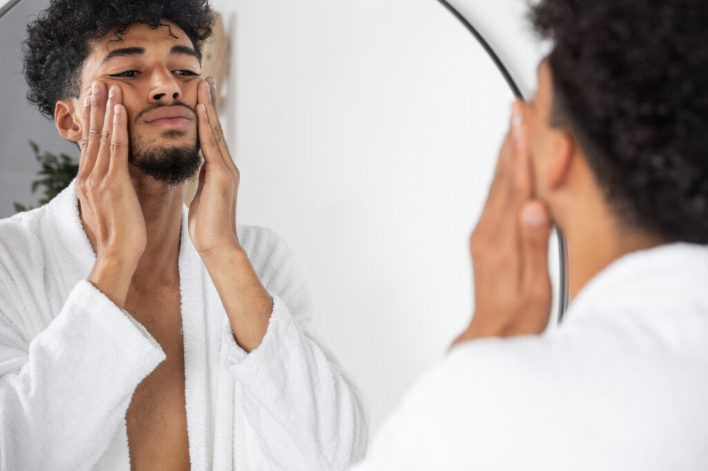 A young man at home looking in the mirror and washing his face after visiting Medical Grade Aesthetics for one of their many medical grade facial near Janesville.