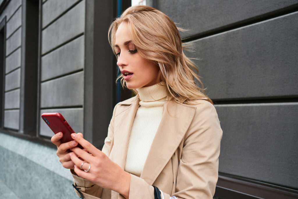 A young woman standing on the sidewalk in the city, booking an appointment at Medical Grade Aesthetic, a high-quality clinic for wellness and aesthetics in Janesville.