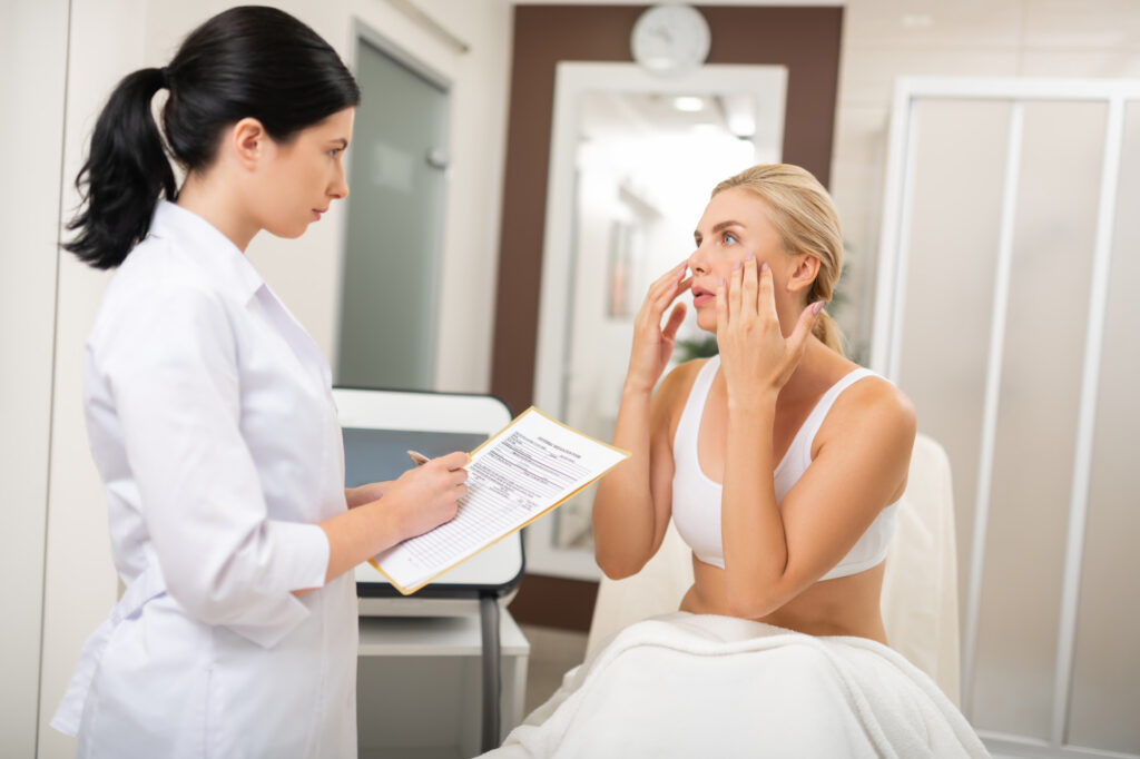 A young blonde woman talking to a caring and dedicated provider from Medical Grade Aesthetics during her consultation, explaining what concerns she would like to address using their options for laser skin treatment in Beloit.