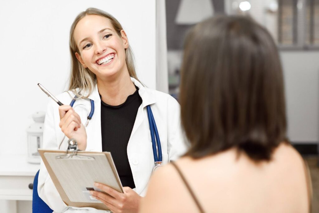A female doctor smiles while taking notes during a discussion with a female patient about Emsculpt NEO near Janesville
