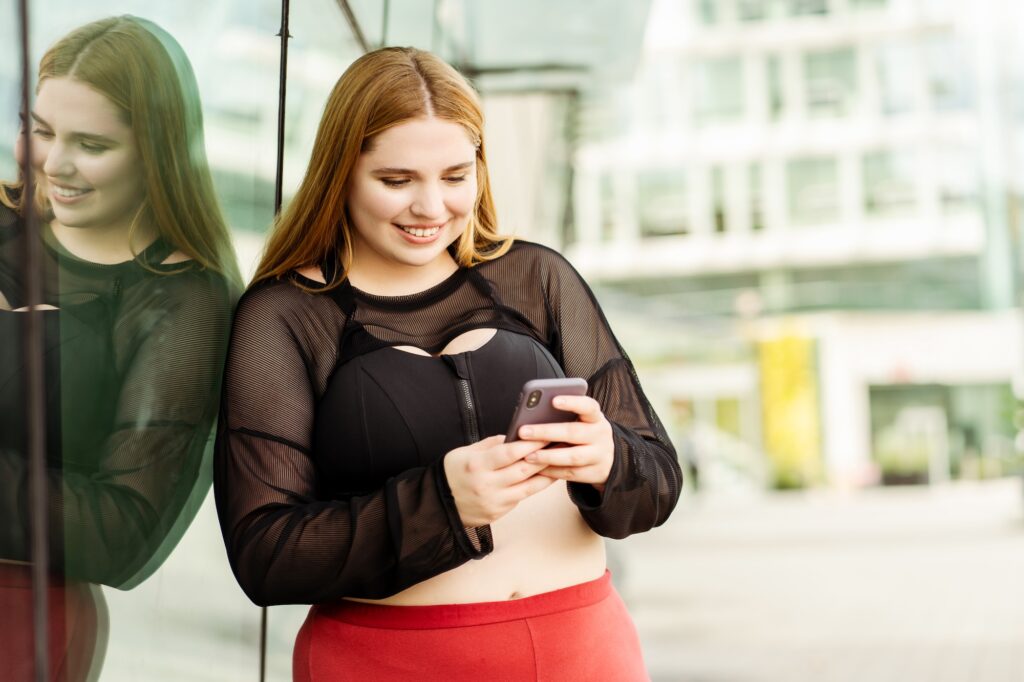 A plus size woman in workout clothes using her phone to look at Medical Grade Aesthetics websites, the premiere weight loss clinic in Janesville.